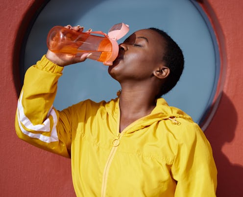 A woman drinks collagen water while wearing a yellow zip up hoodie.