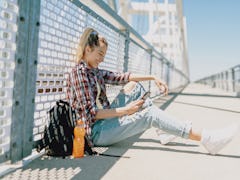 A teenager in the city with backpack looks at some POV TikTok video ideas for back-to-school videos....