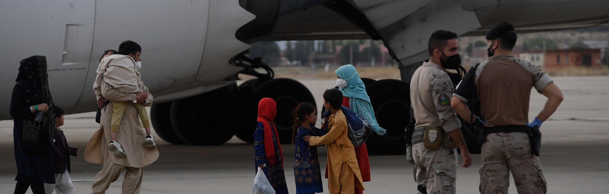 Military personnel stand on the tarmac as refugees disembark from an evacuation flight from Kabul, a...