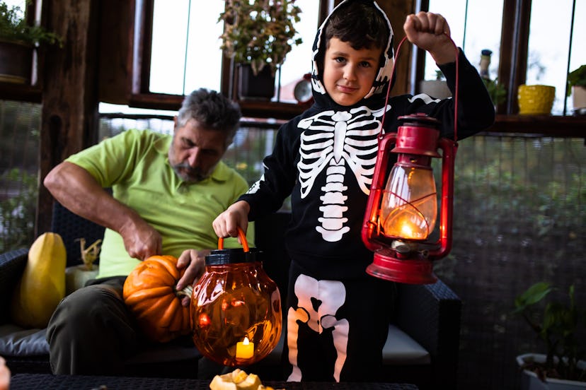 A cute boy in a skeleton costume is holding a plastic Halloween pumpkin, halloween jokes and riddles