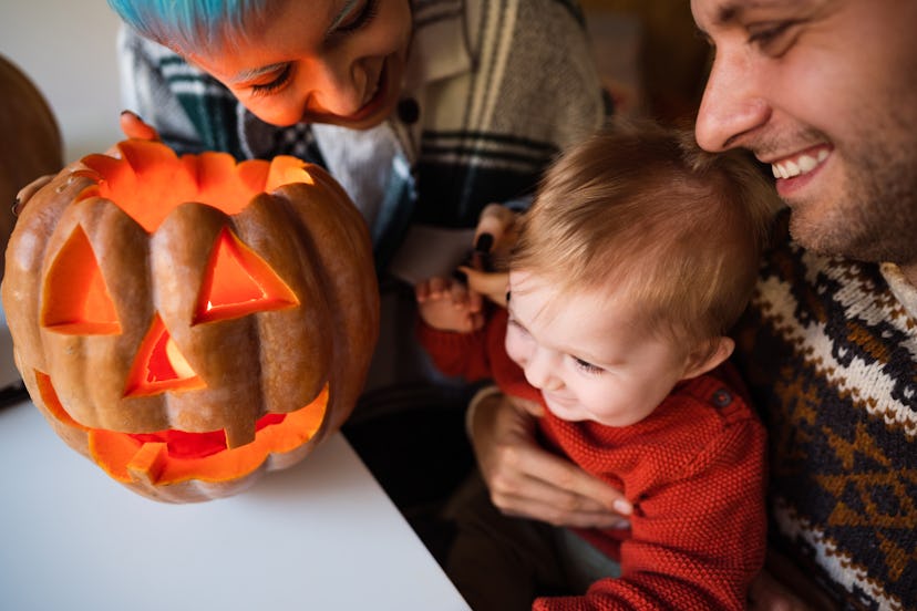 Happy young family of three having fun while decorating a pumpkin for the Halloween holiday.