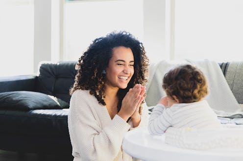 At home in the morning, the mid adult mother smiles as she teaches her unrecognizable baby to clap.