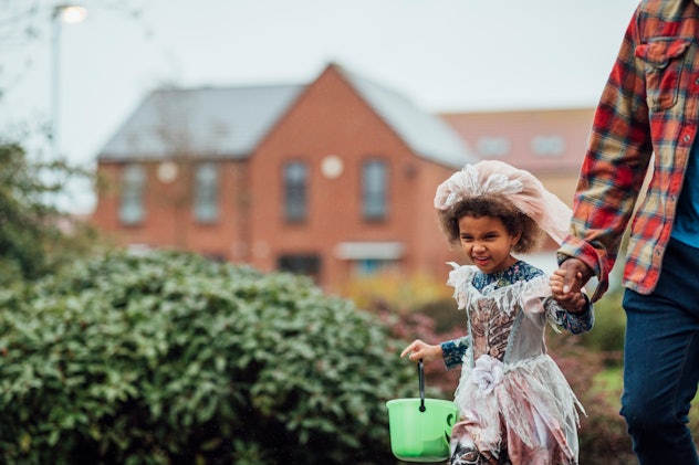 little girl trick-or-treating on halloween holding her dad's hand