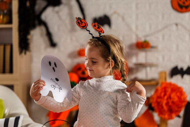 girl holding a ghost mask that she is going wear as a part of her costume for Halloween, halloween j...