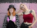 two women smiling at the camera in front of a pink wall, discussing aries libra friendship compatibi...