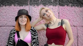 two women smiling at the camera in front of a pink wall, discussing aries libra friendship compatibi...