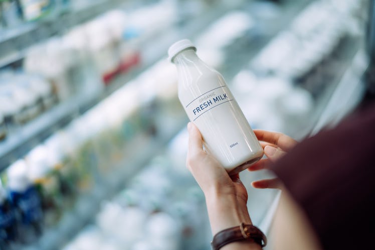 Over the shoulder view of young Asian woman grocery shopping in supermarket. Holding a bottle of org...