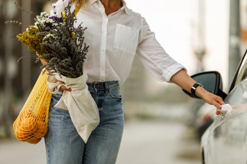 Midsection of unrecognizable woman holding a bouquet of dried flowers and a reusable mesh bag hangin...