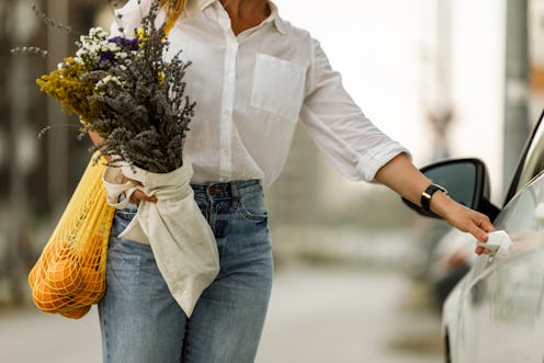 Midsection of unrecognizable woman holding a bouquet of dried flowers and a reusable mesh bag hangin...
