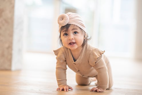 An adorable little girl is crawling forward towards the camera. She is wearing a cute baby turban on...