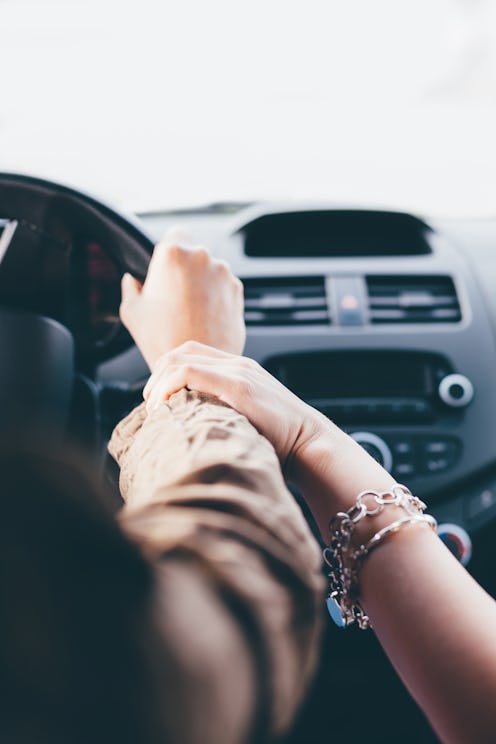 Close up of girl friends traveling by car and holding hands in a road trip.