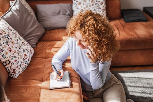 Young woman talking on the phone at home and writing notes in living room