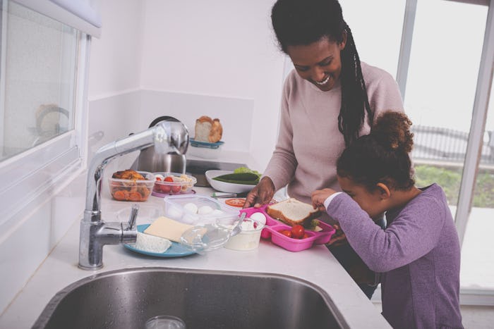 A young mother and her 6 years old girl preparing breakfast and lunch for school and work. Curious l...