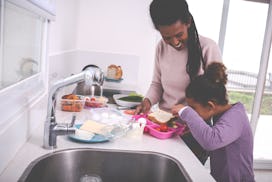 A young mother and her 6 years old girl preparing breakfast and lunch for school and work. Curious l...
