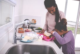 A young mother and her 6 years old girl preparing breakfast and lunch for school and work. Curious l...