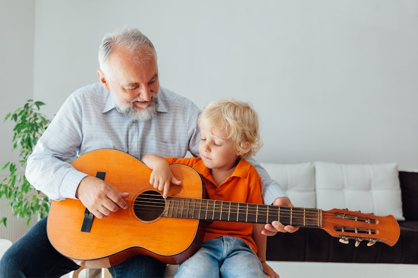 Happy grandpa teaching his grandson to play guitar.