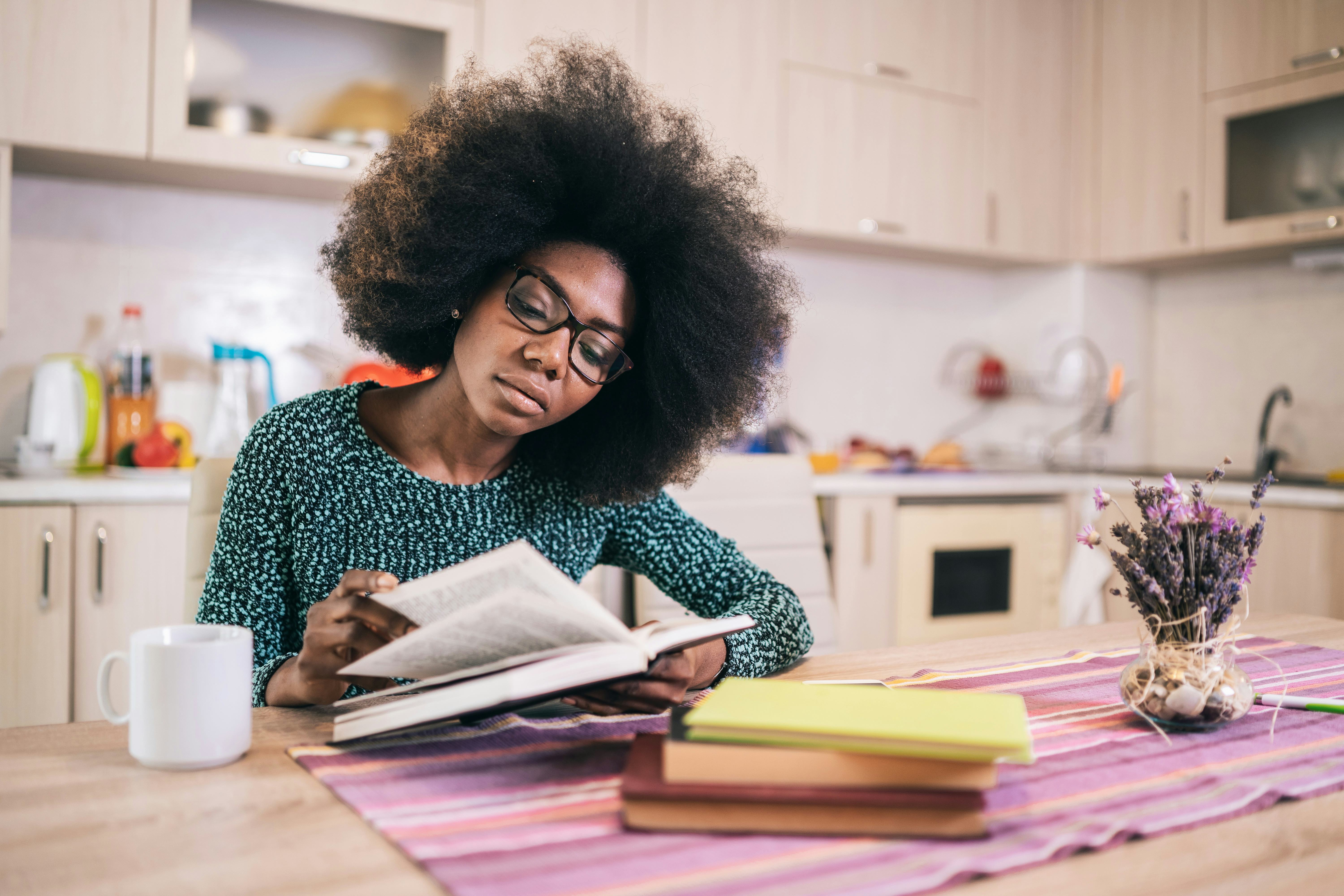 Portrait of attractive african american young woman sitting in the kitchen reading book