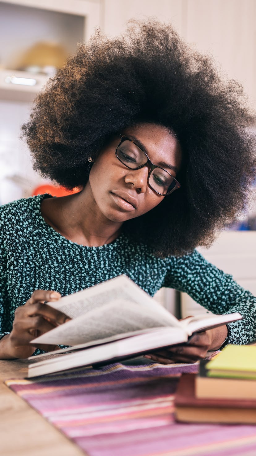 Portrait of attractive african american young woman sitting in the kitchen reading book