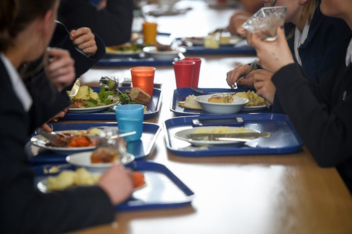 Students eat their school dinner from trays and plates during lunch in the canteen at Royal High Sch...