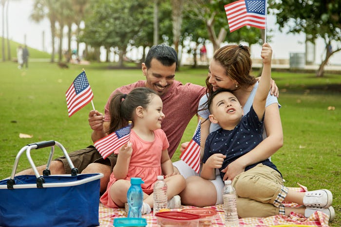 Young Miami family with 4 and 6 year old children holding American flags while enjoying weekend picn...