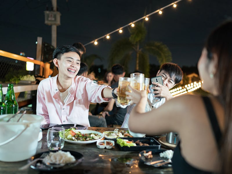 Group of young Asian friends having party drinking beer and eating Thai food in outdoors restaurant,...