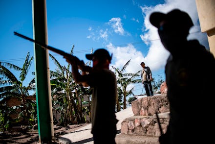 A boy aims a rifle as the Regional Coordinator of Community Authorities (CRAC-PF) community police f...