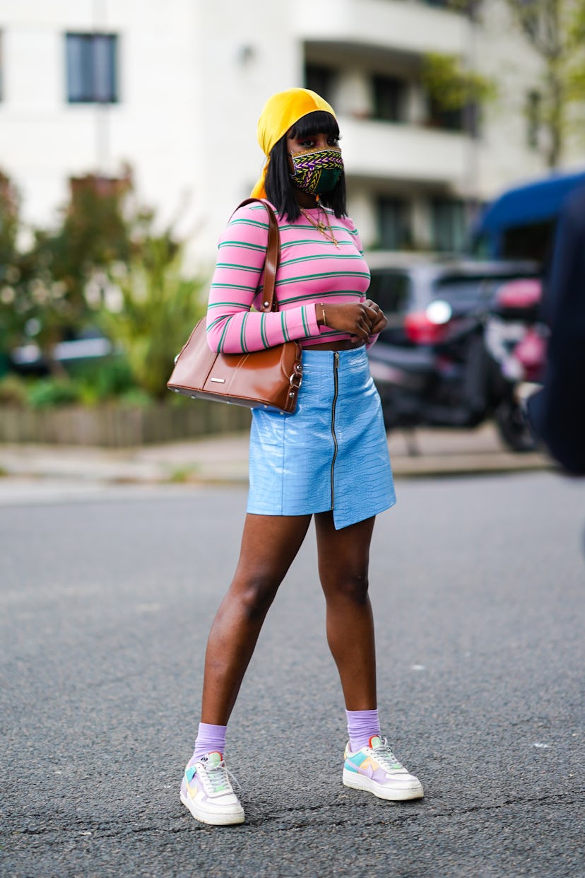 A young Black woman wears an asymmetrical blue leather skirt paired with a green and pink striped to...