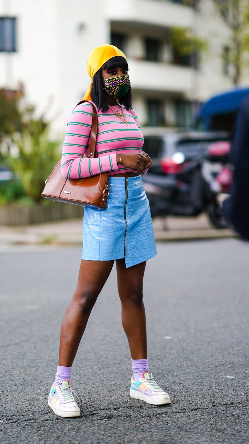 A young Black woman wears an asymmetrical blue leather skirt paired with a green and pink striped to...