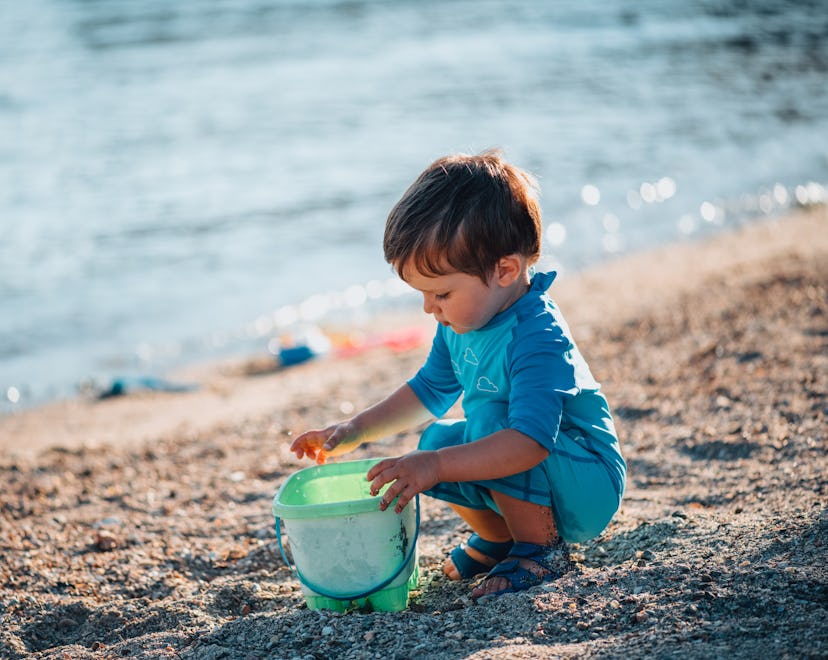 Baby Boy Plays With Toy Bucket in the Sea