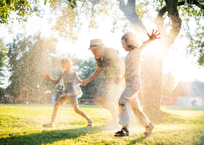 Small boy and girl with grandfather running through water sprinkler.