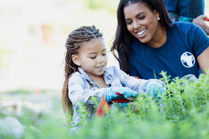 A mom smiles as her young daughter clips herbs from an herb garden.