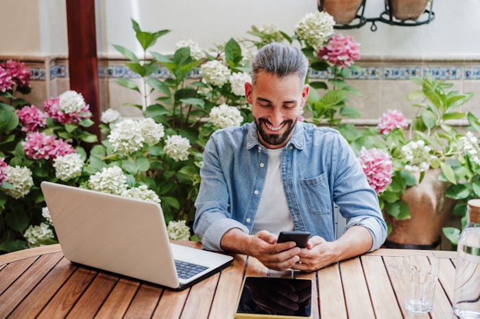 man looking at phone while on laptop