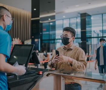 Asian Chinese male customer with facemask buying popcorns drink contactless payment before movie sho...