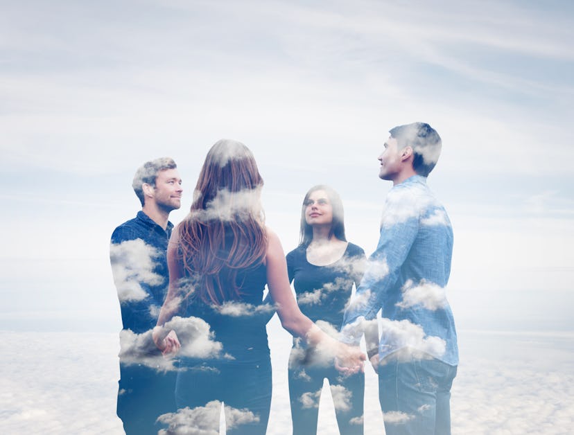 Double exposure of four friends holding hands with clouds.