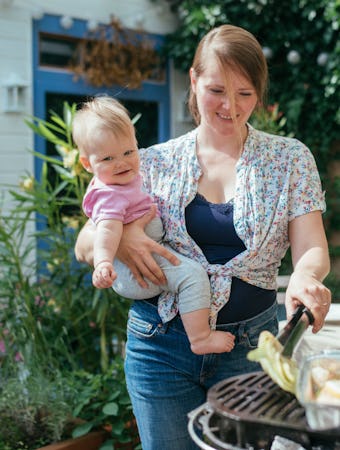 Smiling woman holding her daughter while doing vegan bbq at home outdoor.
