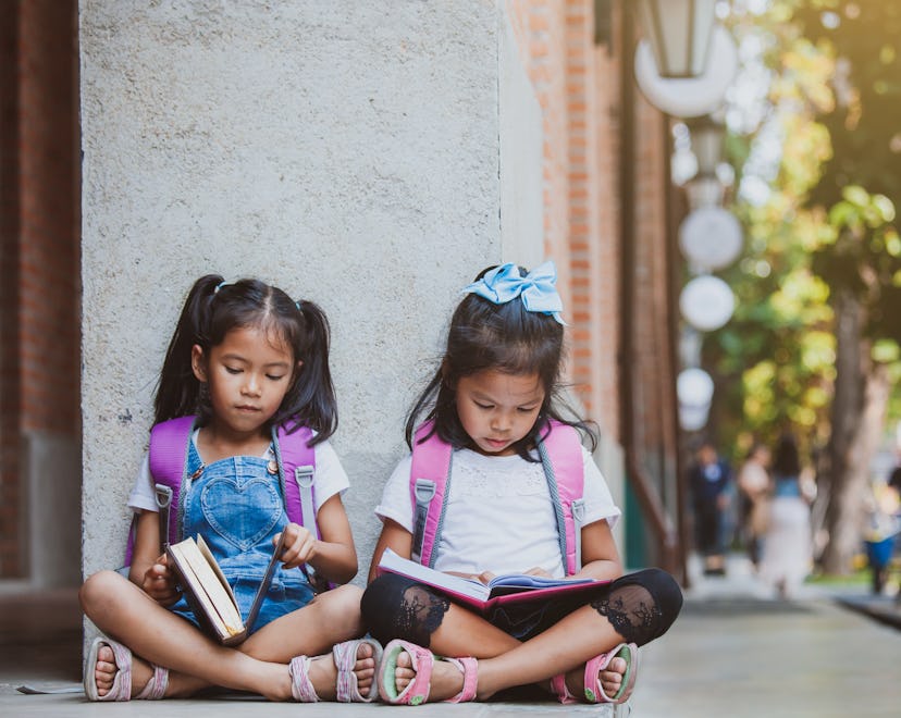 Twin girls sitting next to each other on the ground reading books