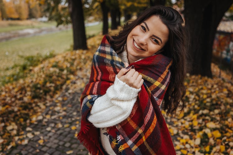 Beautiful smiling young woman in white sweater enjoying autumn walk on the city promenade on sunny d...