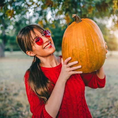 Young smiling woman holding pumpkin for Halloween outdoors during the 2021 fall equinox, which will ...