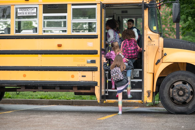 Kids wearing backpacks, getting on a school bus. 
