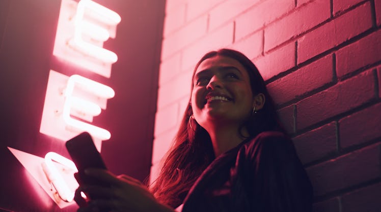 Shot of a young woman using her cellphone while outside a building at night