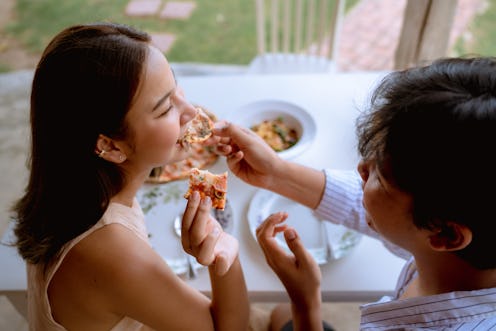 Young Asian couple sharing pizza and eating together at restaurant in holiday.