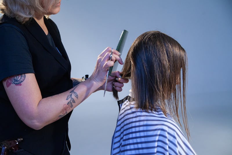 High angle of crop female hairdresser cutting hair of anonymous female client in beauty salon