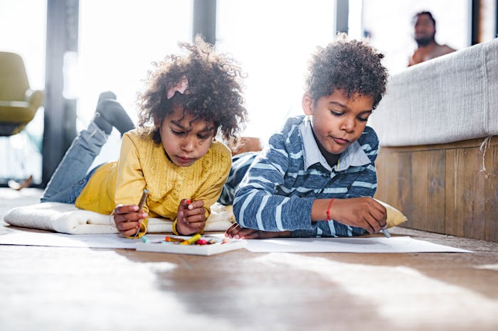 Two kids lying on the floor, coloring on pieces of paper