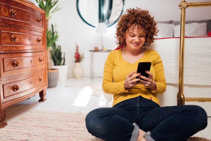Attractive young Caucasian woman enjoying herself at home, using a smart phone and smiling