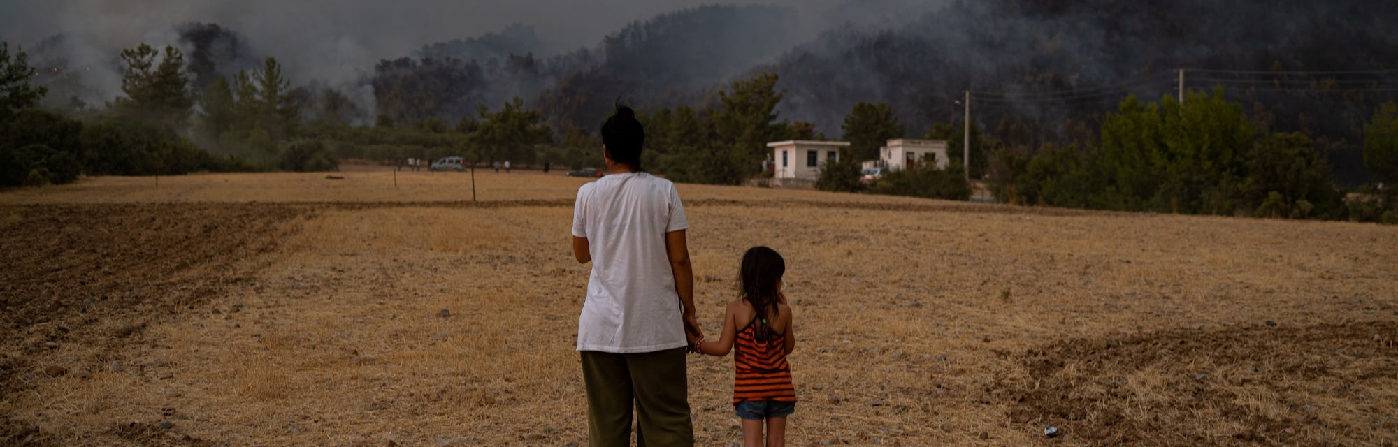 TOPSHOT - A woman and child stand in a field as they watch wildfires as they burn in Koycegiz distri...