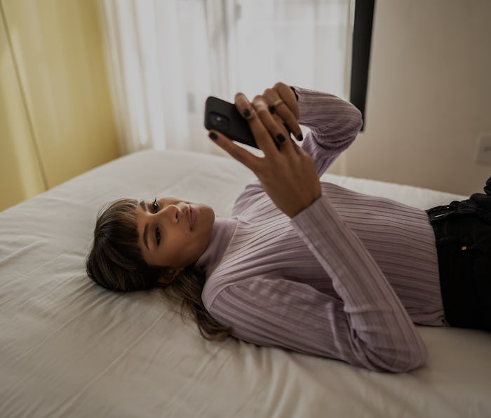 Happy young woman using smartphone lying on the bed at home