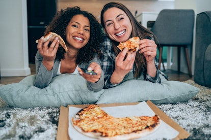 Two sorority sisters in the same pledge family lie on the floor eating pizza and watching TV, which ...