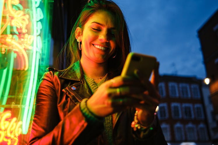Young woman texting in neon lights during Mercury retrograde fall 2021, which will affect her zodiac...