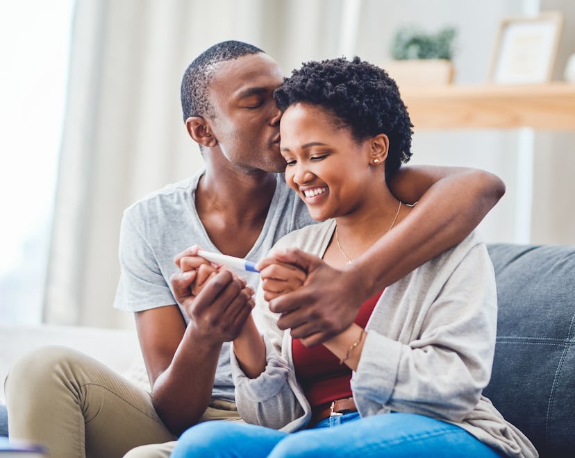 Cropped shot of a young couple embracing, kissing and holding hands as she holds a positive pregnanc...