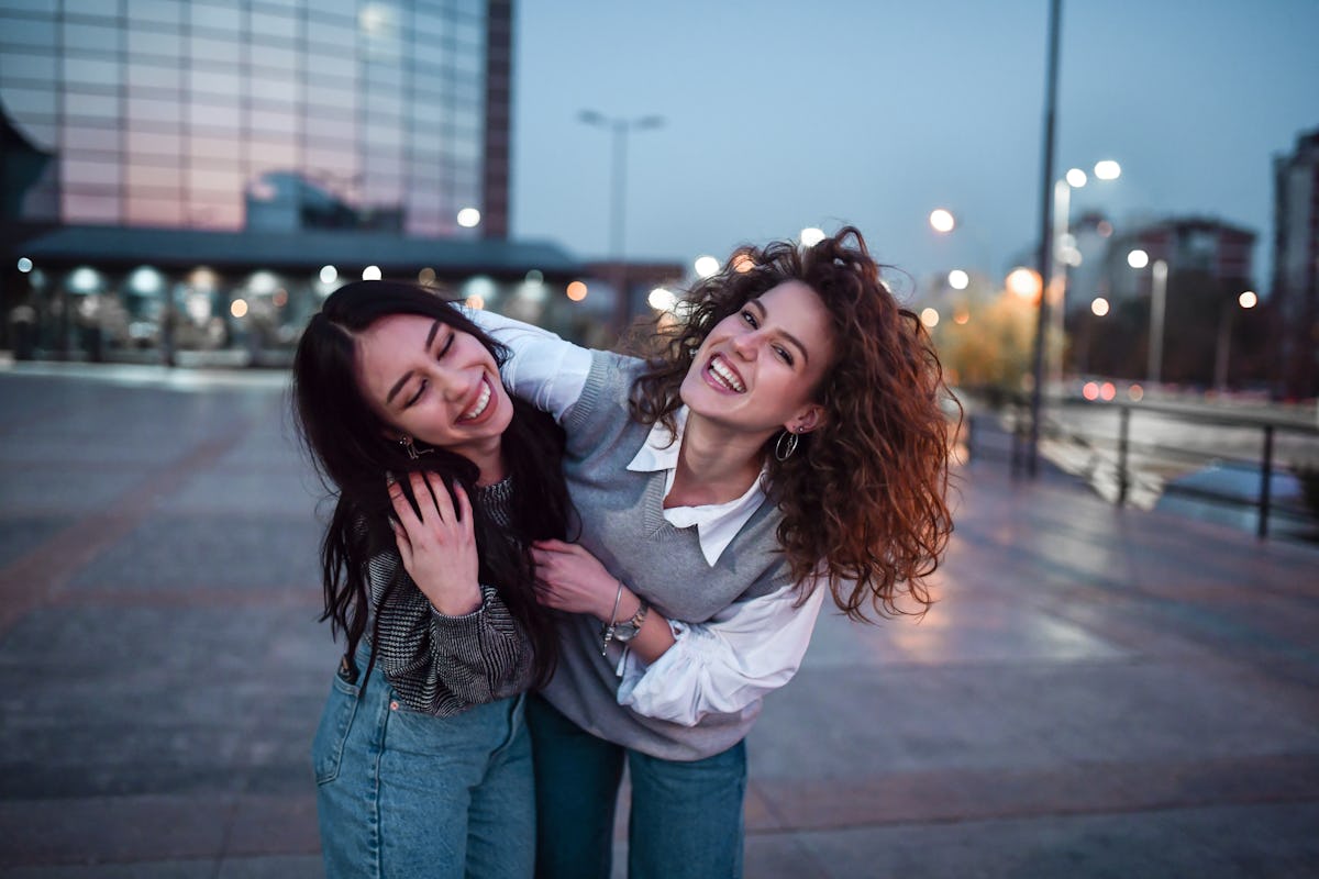Belas mulheres abraçando andando fora do prédio de apartamentos à noite